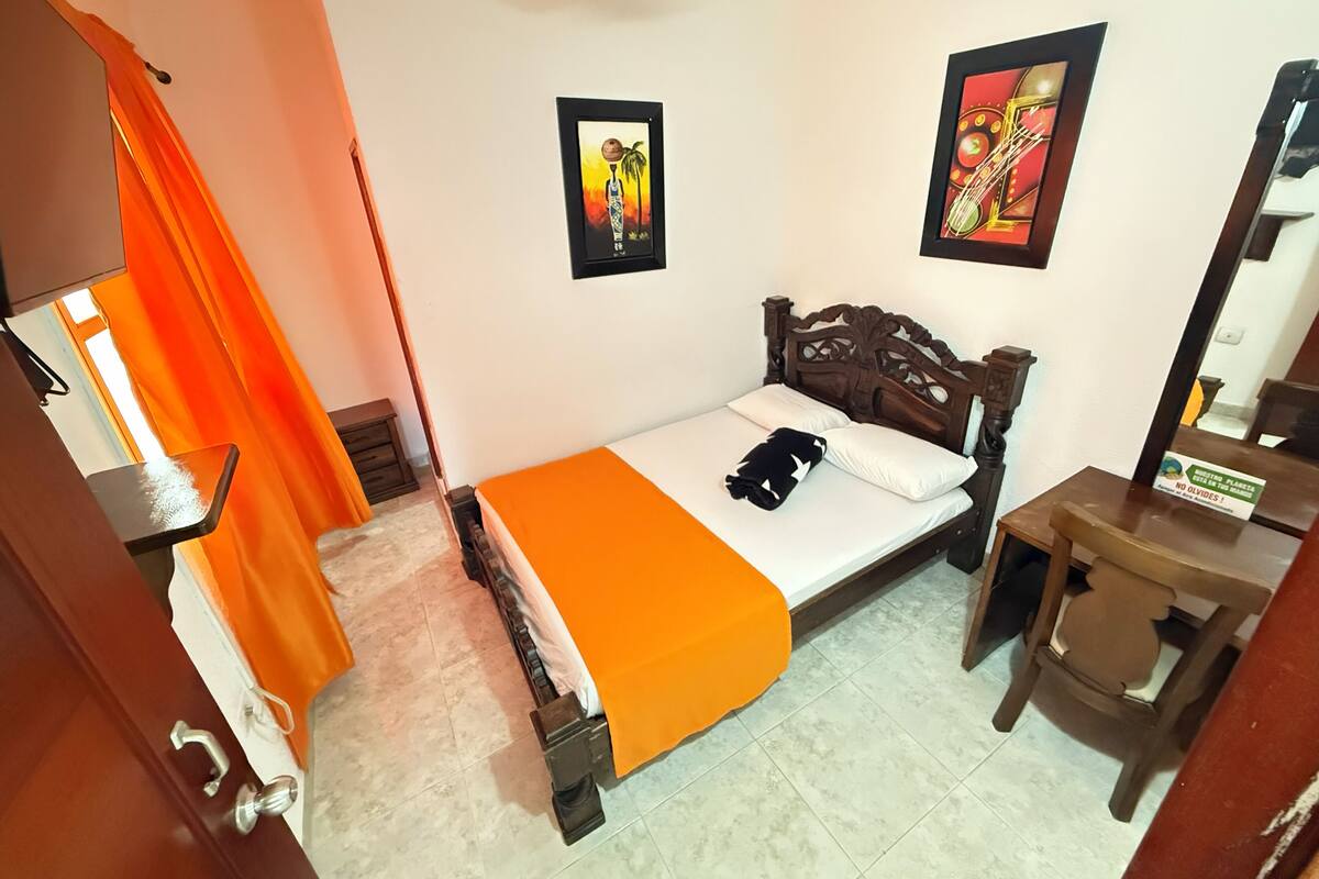 A bedroom with a bed, a wooden headboard, a nightstand, a mirror, and two framed pictures on the wall.
