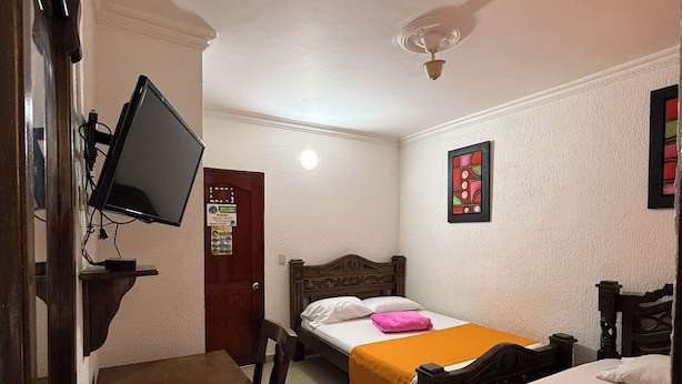 A hotel room with two beds, a desk, a chair, a television, and a ceiling fan. - Hotel La Casa del Turista (Cartagena)