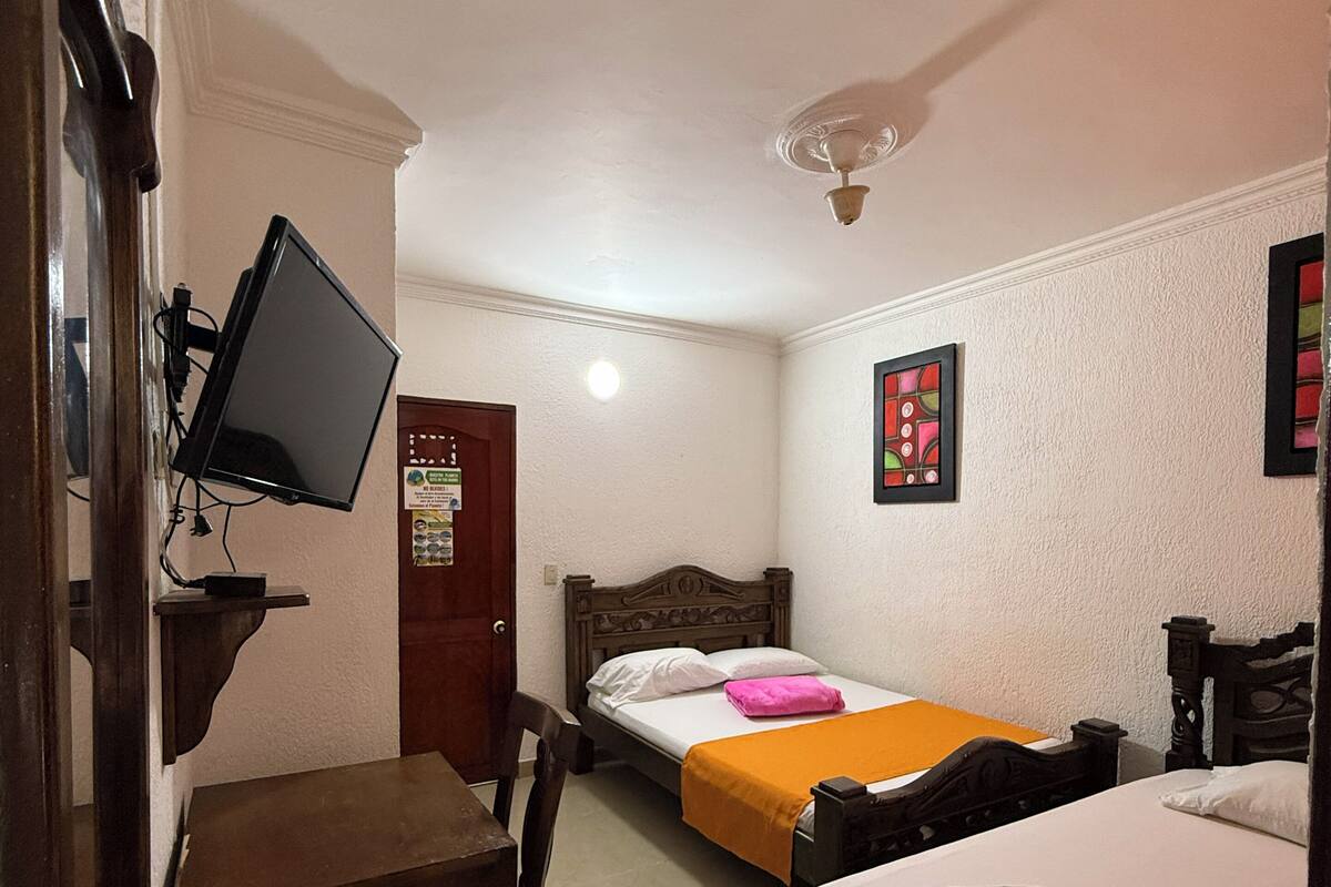 A hotel room with two beds, a desk, a chair, a television, and a ceiling fan.