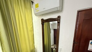 A room with a wooden chair, a small table, a mirror, a door, and an air conditioning unit. - Hotel La Casa del Turista (Cartagena)