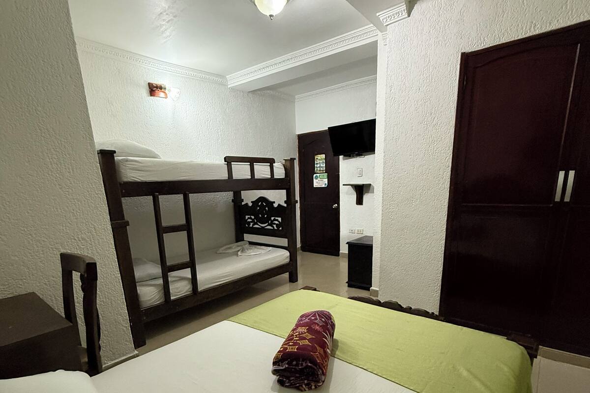 A room with bunk beds, a green mat, a bed with a rolled-up blanket, a wooden nightstand, a TV, and a wardrobe.