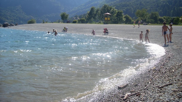 A beach with people swimming and walking along the shore, surrounded by mountains. - Garnì Lago Alpino (Molveno)