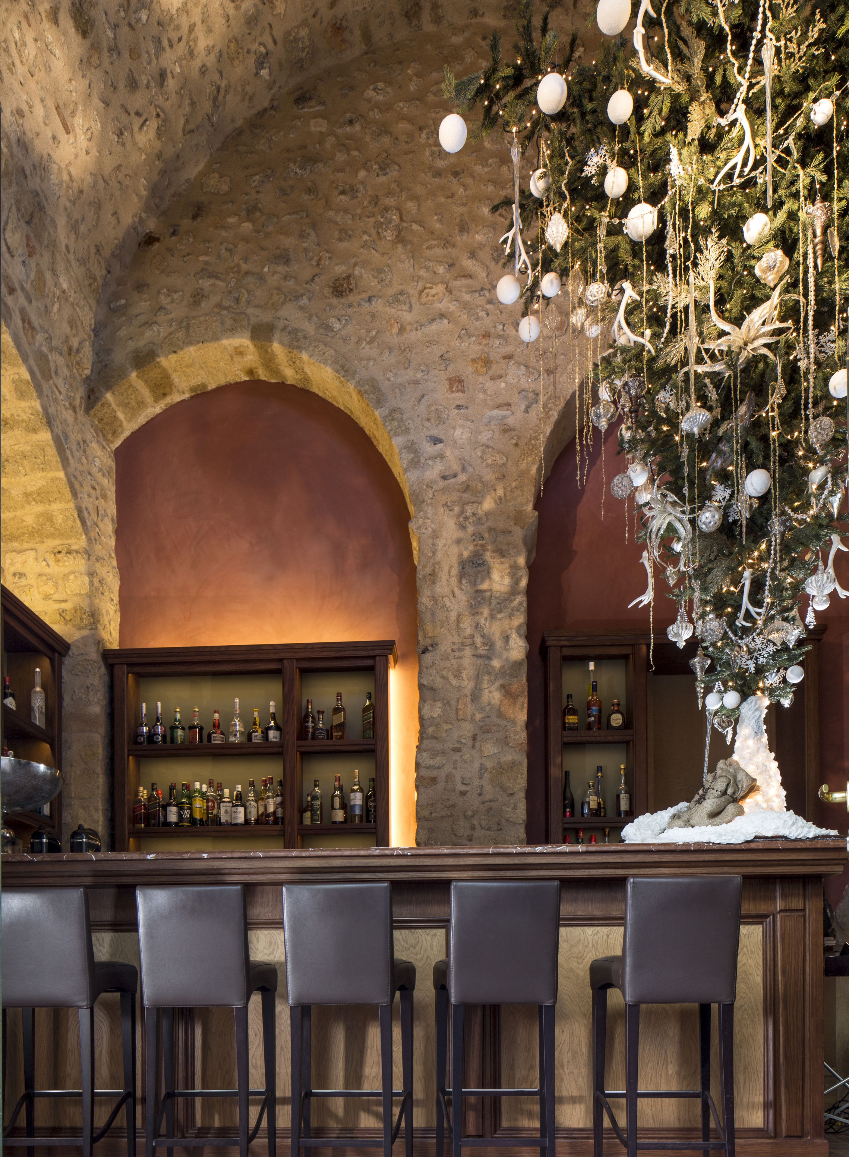 A bar area with stone arches, a Christmas tree, and shelves of liquor bottles.