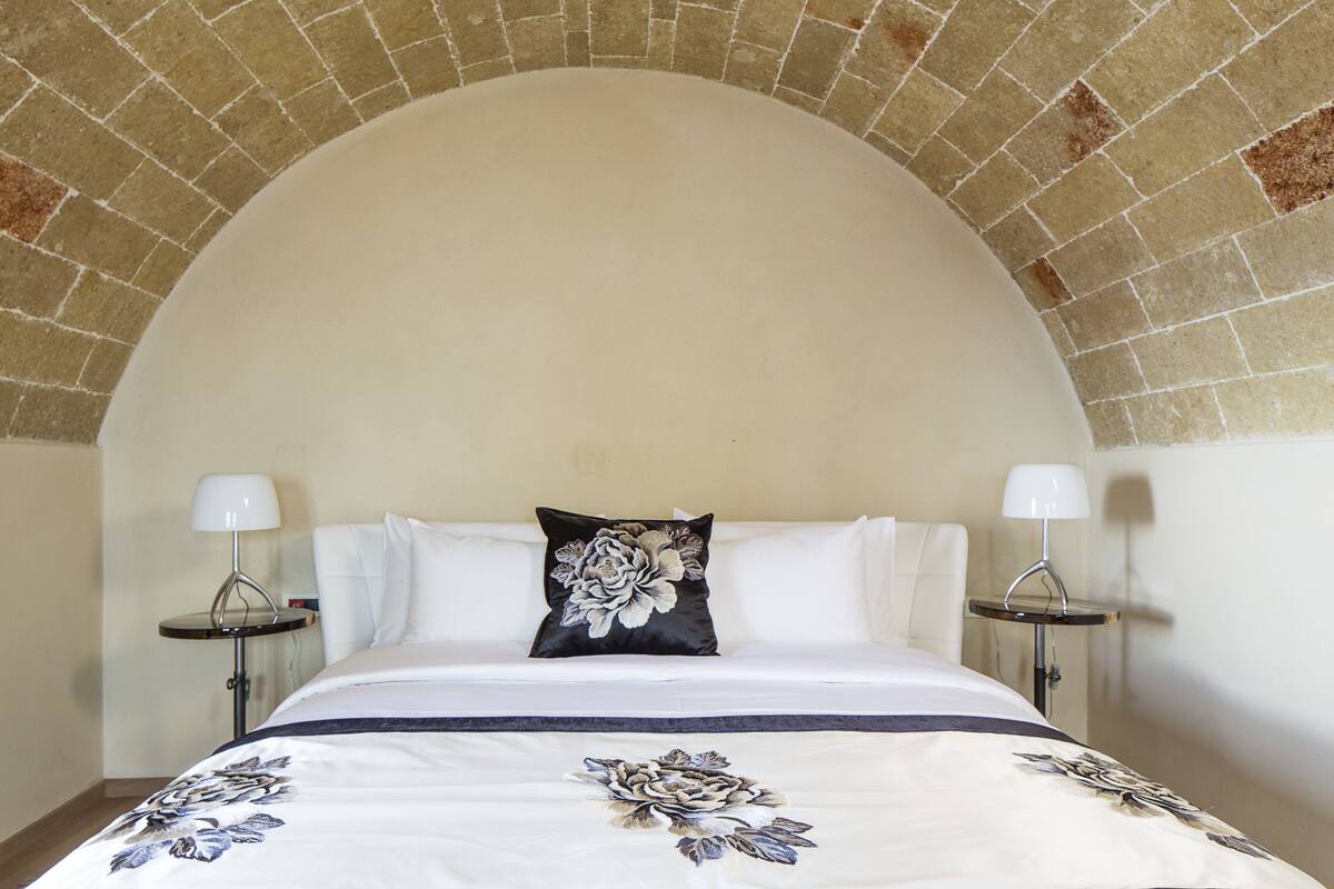 Una habitación de hotel con una cama grande, dos mesitas de noche con lámparas y una colcha con estampado floral.