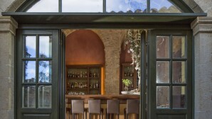 A bar area with a stone wall, wooden bar stools, and shelves with bottles. - Moni Emvasis Luxury Suites (Monemvasia)