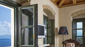 A room with a wooden ceiling, a table with a lamp, and a view of the sea. - Moni Emvasis Luxury Suites (Monemvasia)