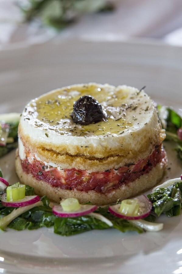 A layered dish with a garnish on top, served on a white plate with a green salad. - Moni Emvasis Luxury Suites (Monemvasia)