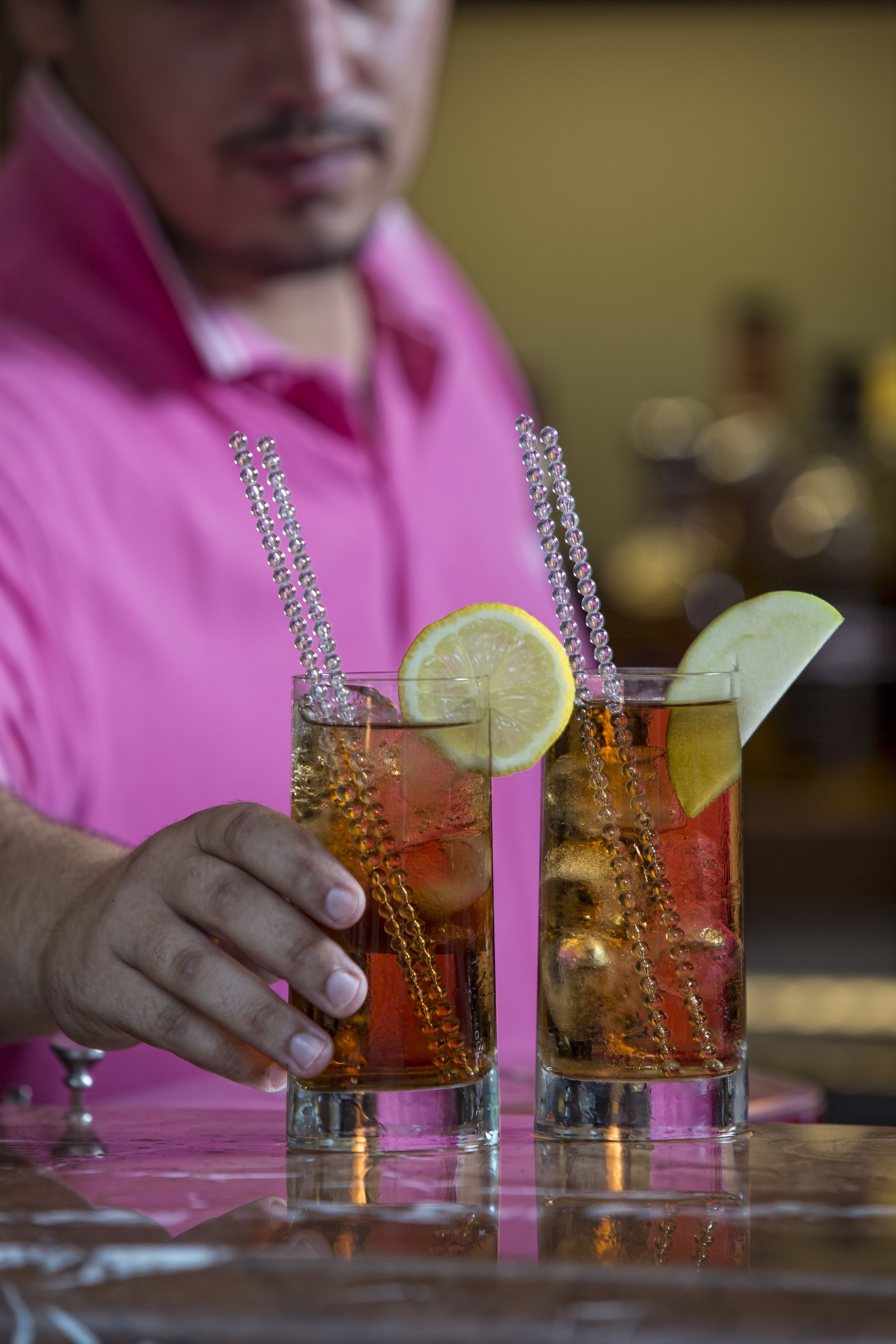 Two glasses of iced tea with lemon slices and straws on a reflective surface.