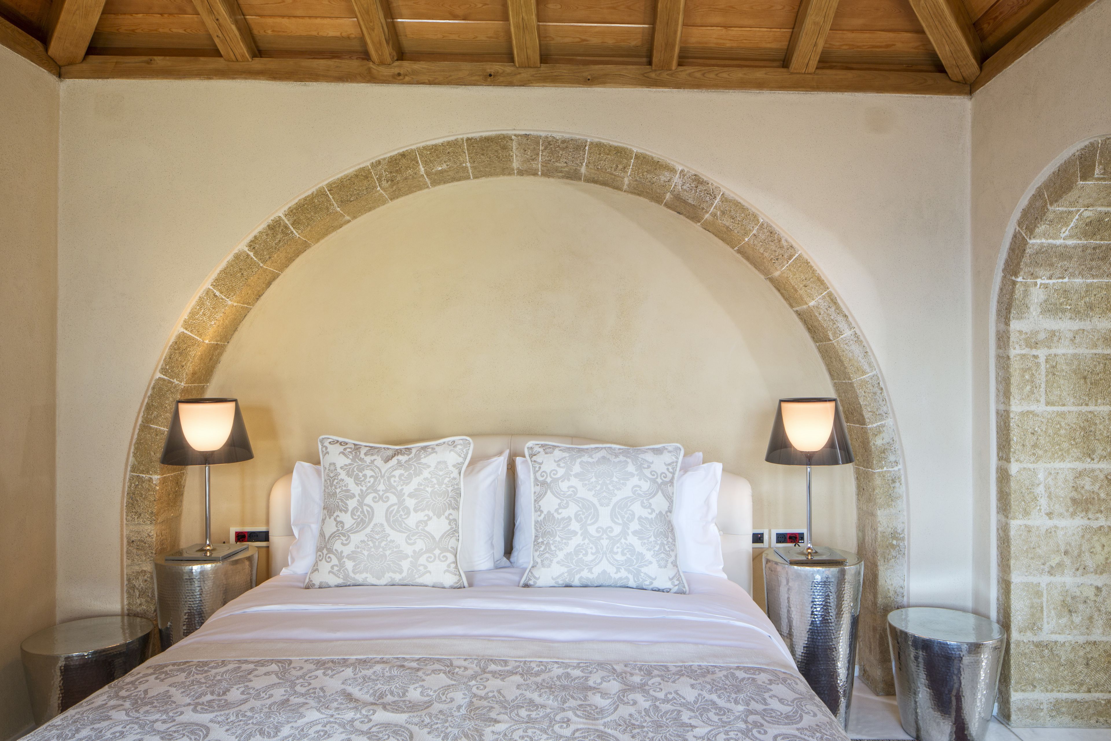A bed with a patterned bedspread, two matching pillows, and two bedside lamps.