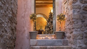 A stone building with a wooden door and a lit wall lamp. - Moni Emvasis Luxury Suites (Monemvasia)