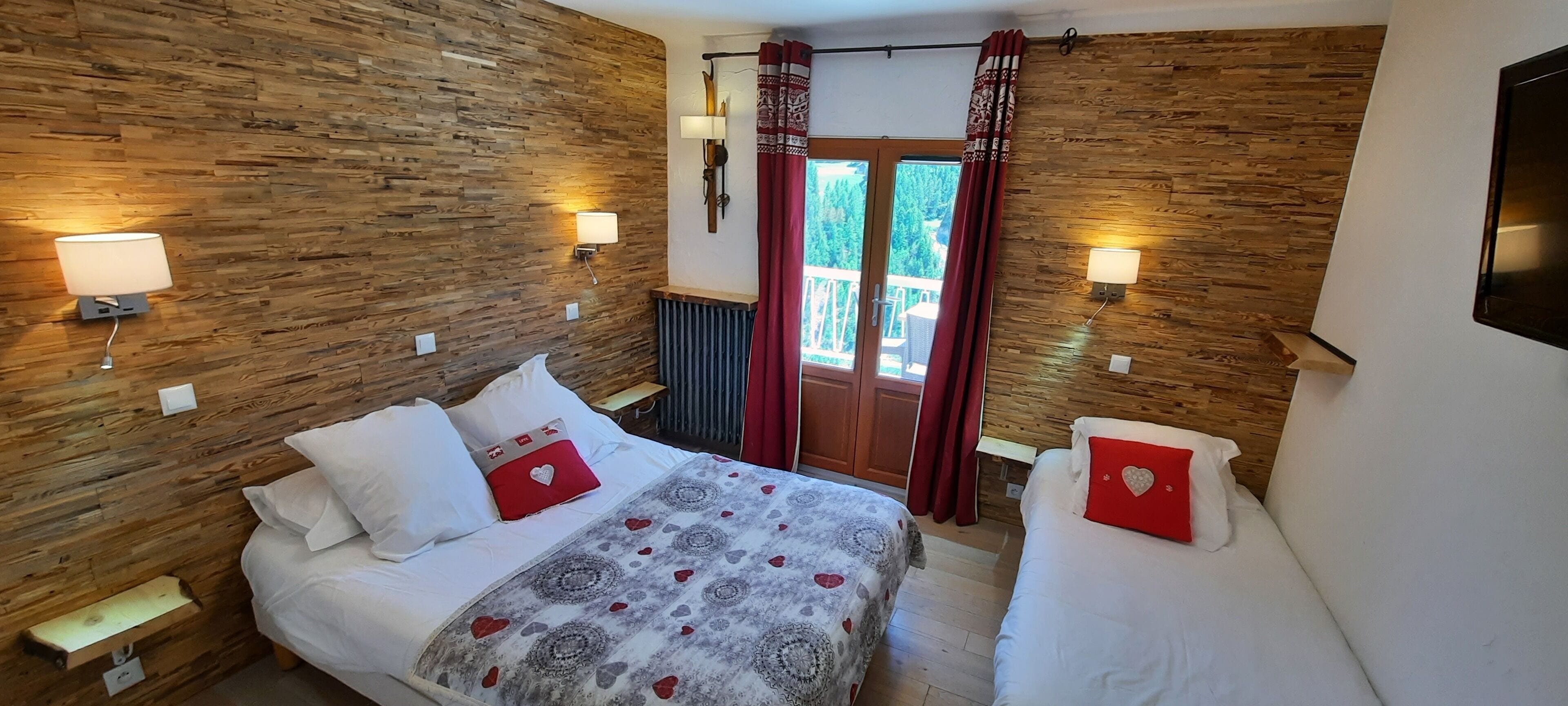 Une chambre avec deux lits, un lambris en bois et un balcon agrémenté de rideaux rouges.