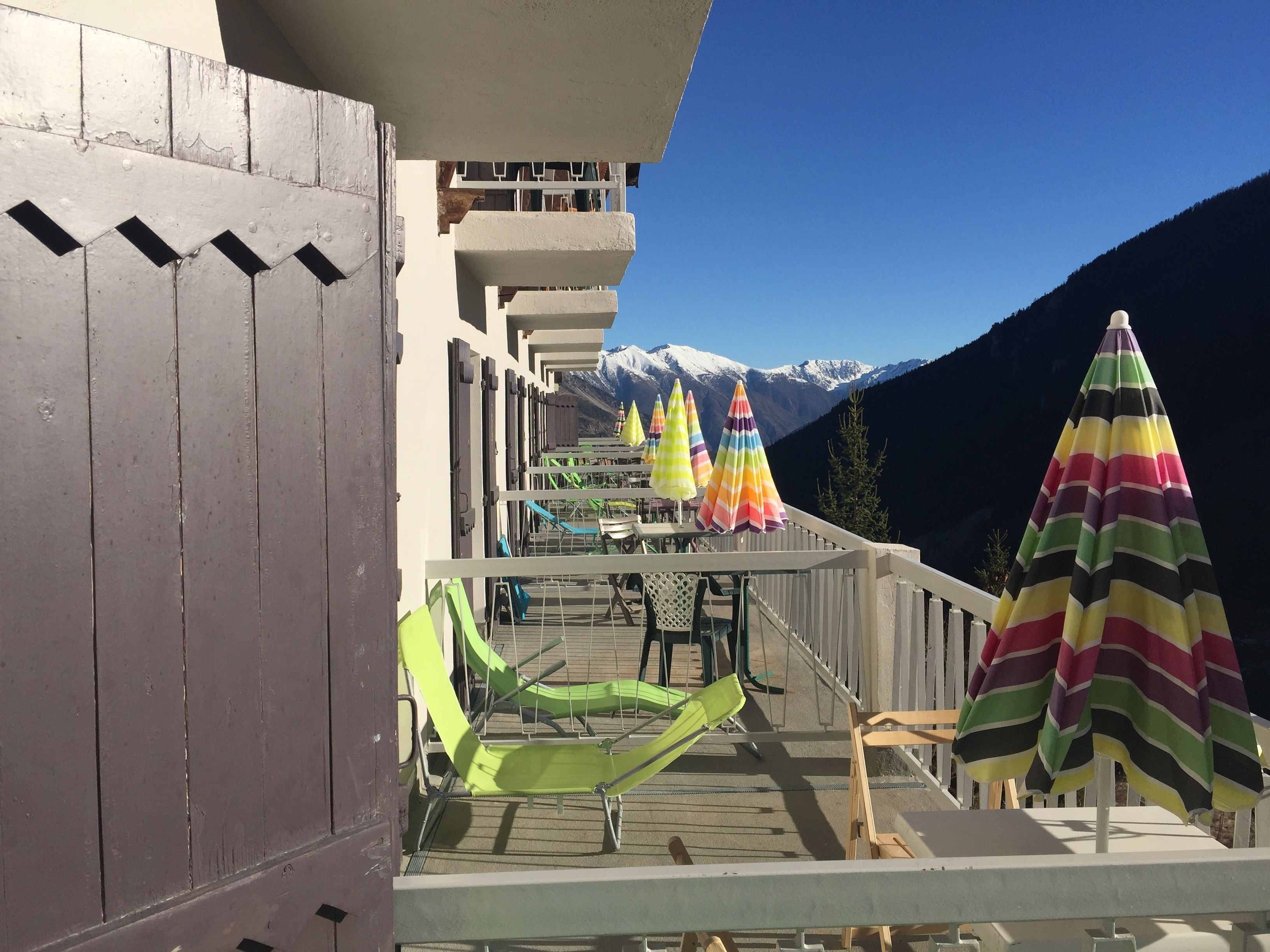 A balcony with green lounge chairs and colorful striped umbrellas, overlooking a mountainous landscape.