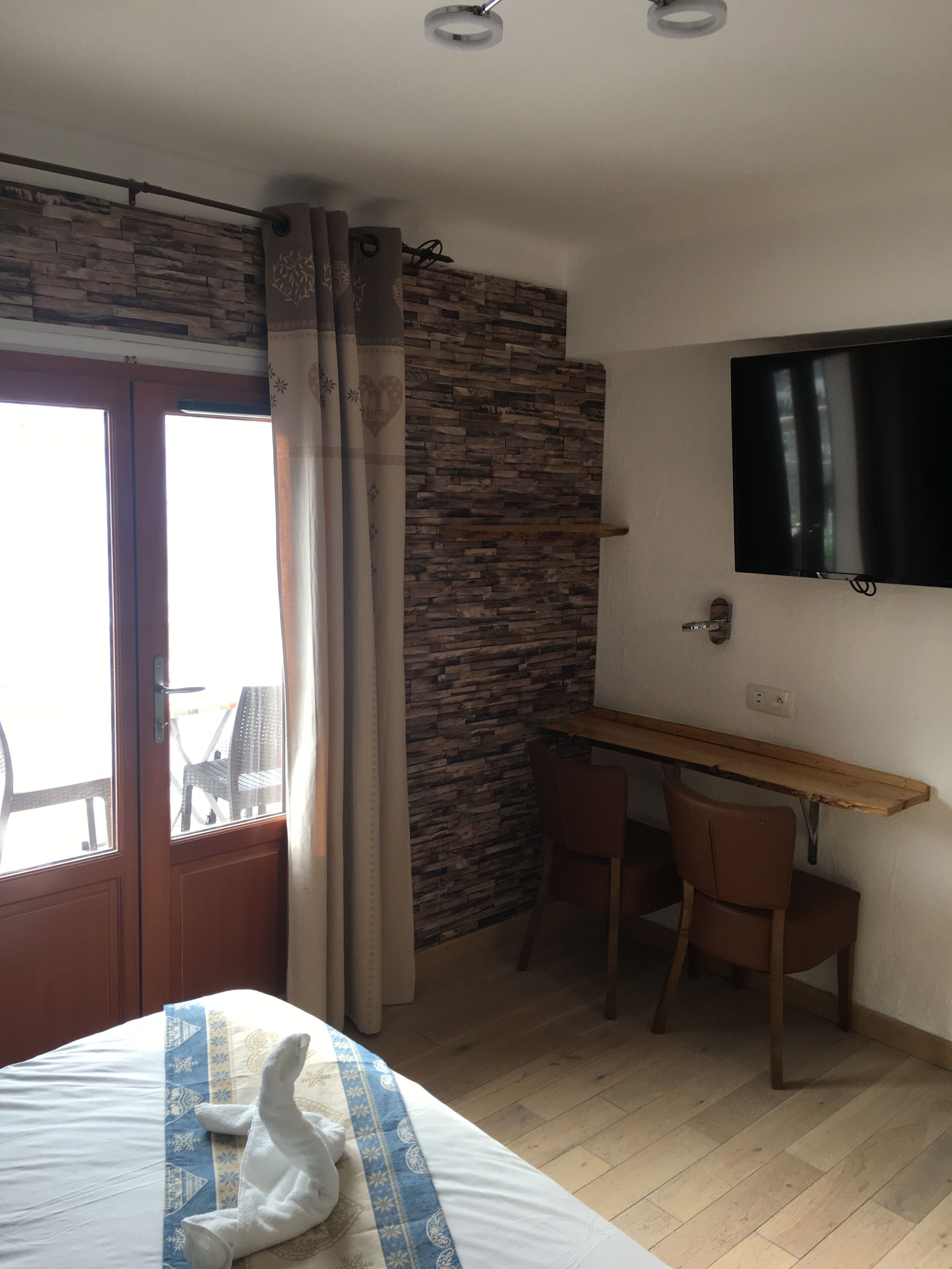 Une chambre d’hôtel comprenant un lit, un bureau avec une chaise, un téléviseur fixé au mur et une fenêtre avec des rideaux.