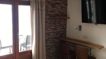 Une chambre d’hôtel comprenant un lit, un bureau avec une chaise, un téléviseur fixé au mur et une fenêtre avec des rideaux.