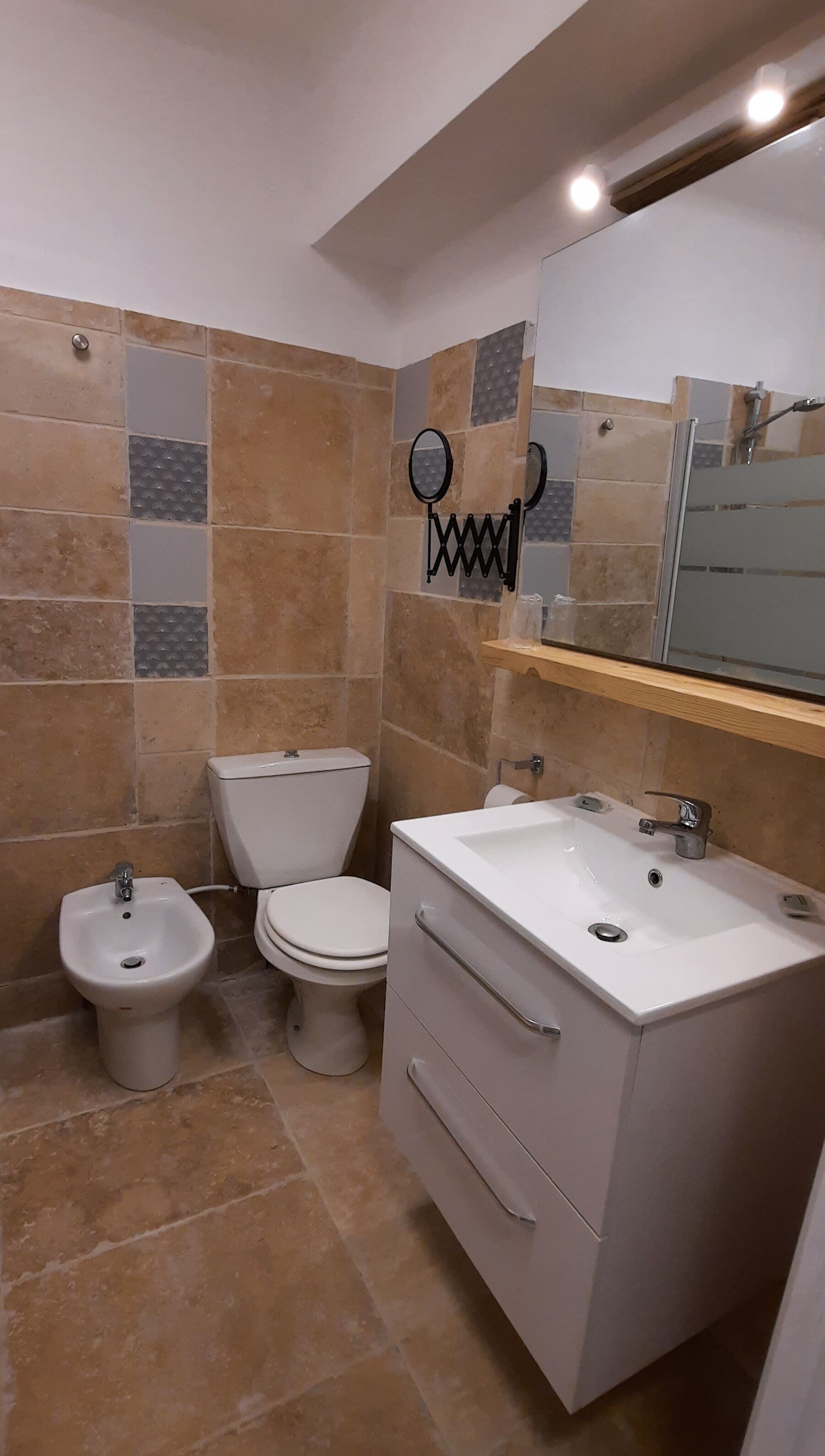 Een badkamer met toilet, bidet, wastafel met spiegel en betegelde wanden.