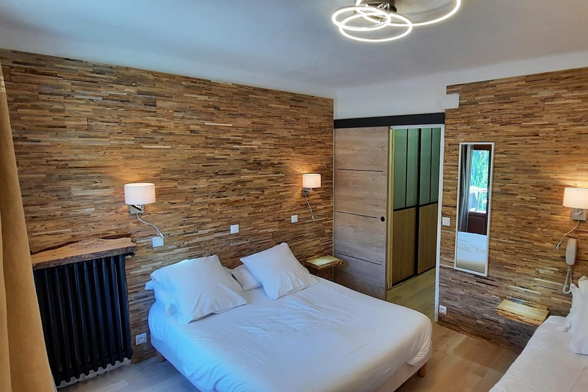 A modern bedroom with a wooden wall design, a bed with white bedding, bedside lamps, and a mirror.