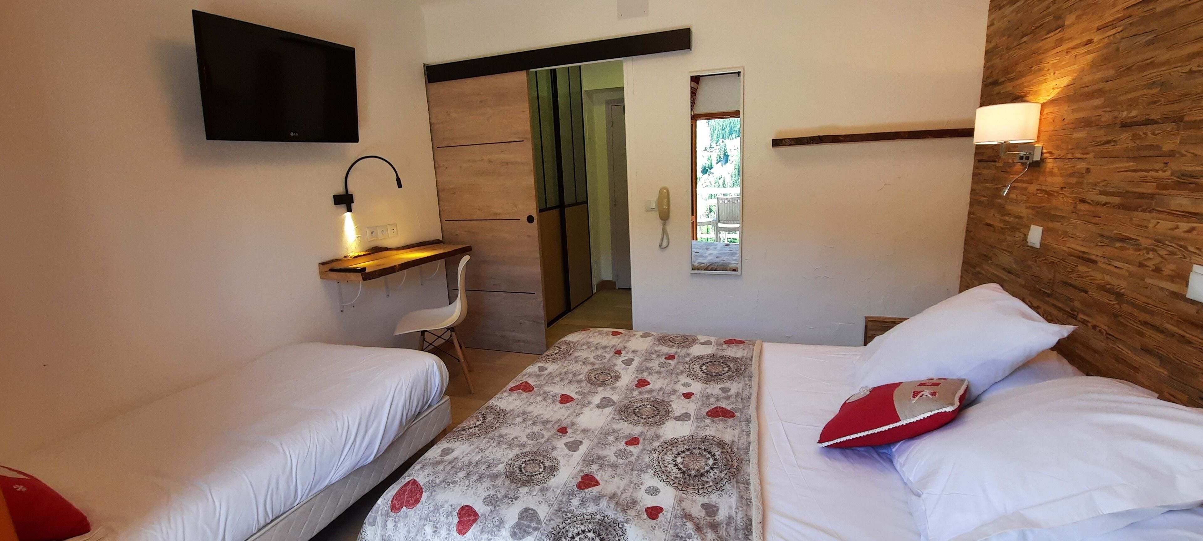 A hotel room with two beds, a desk with a lamp, a mirror, and a wooden accent wall.