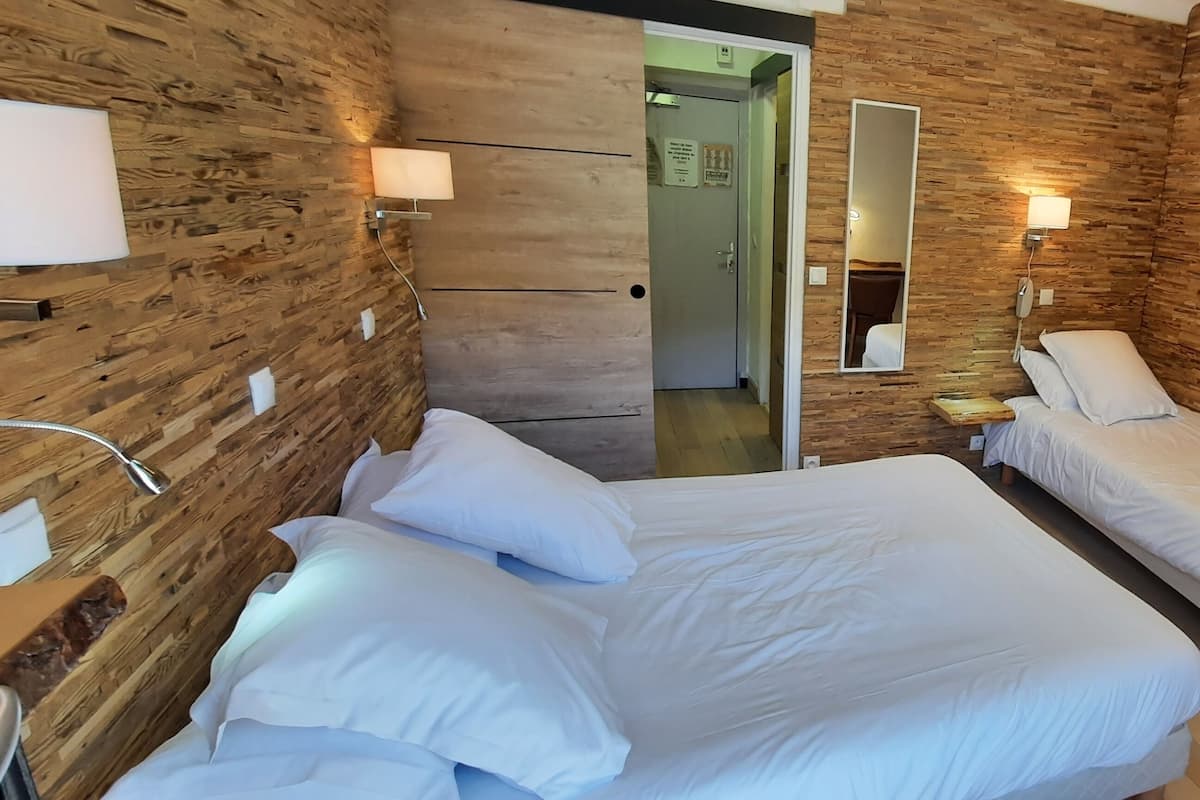 A hotel room with two beds, wooden walls, a TV, and a bedside table with a lamp.