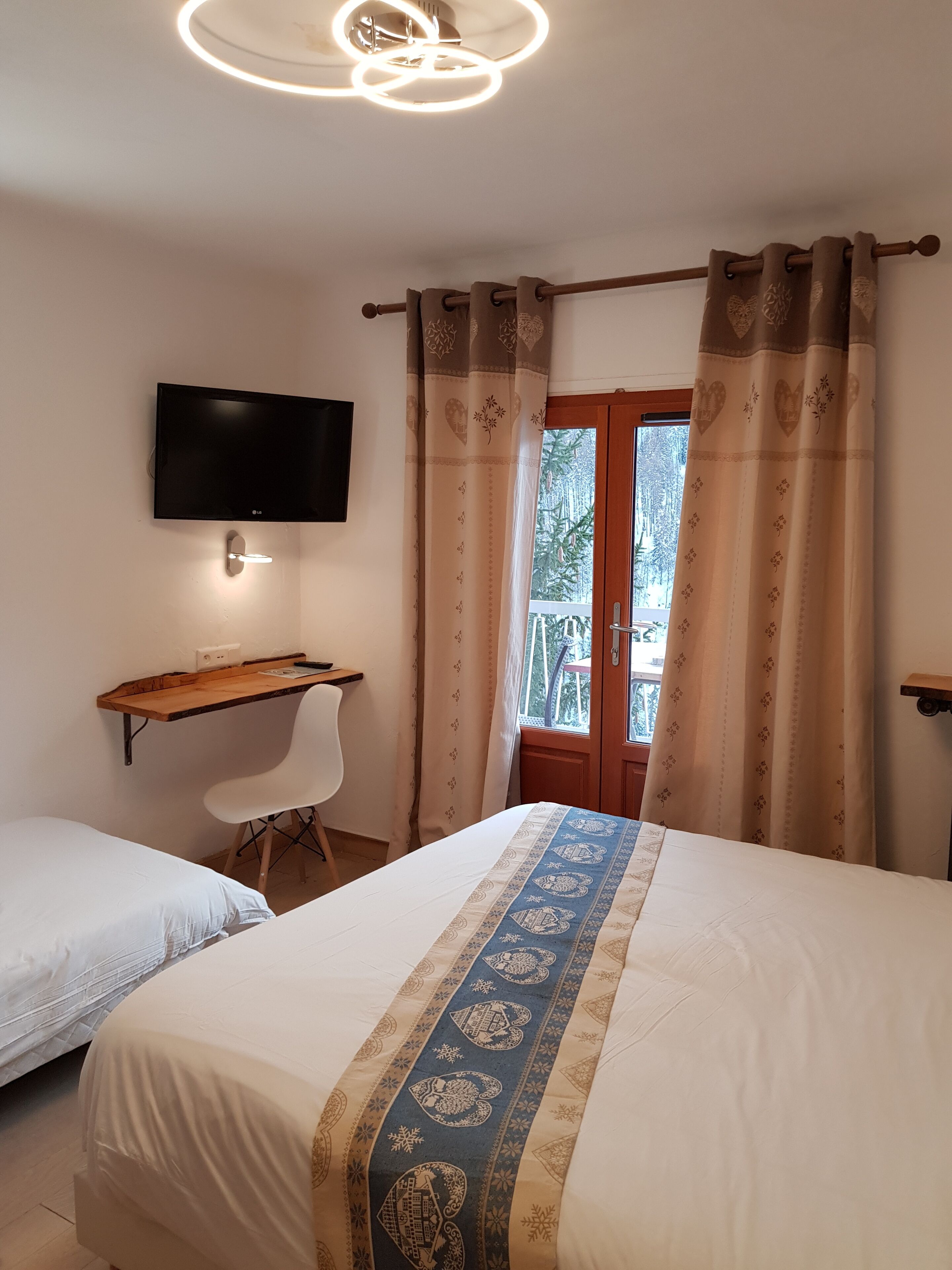 A bedroom with a bed, a desk, a chair, a TV, and a window with curtains.