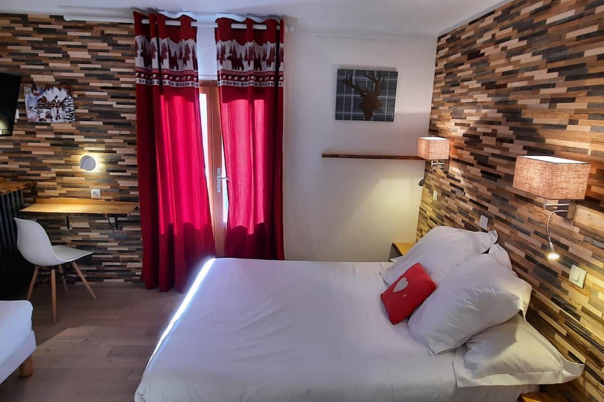 A hotel room with a bed, a desk, a chair, a TV, and a wall with a wooden pattern.