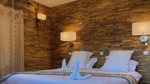 A hotel room with a wooden wall panel design, two bedside lamps, a bed with white bedding, and a decorative towel arrangement.