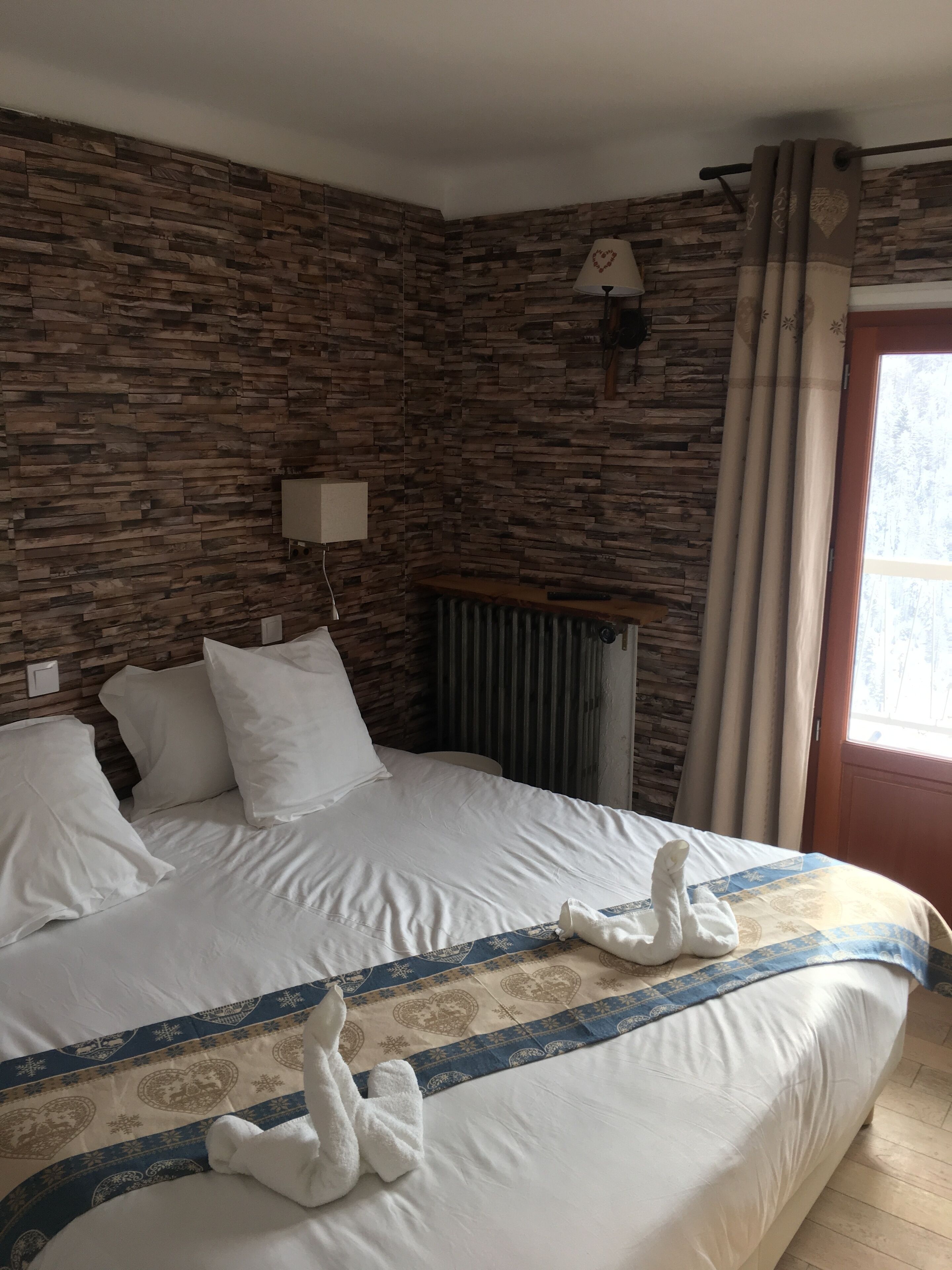 Et hotelværelse med en seng, hvide puder, et mønstret sengetæppe og en væg med træpaneldesign.