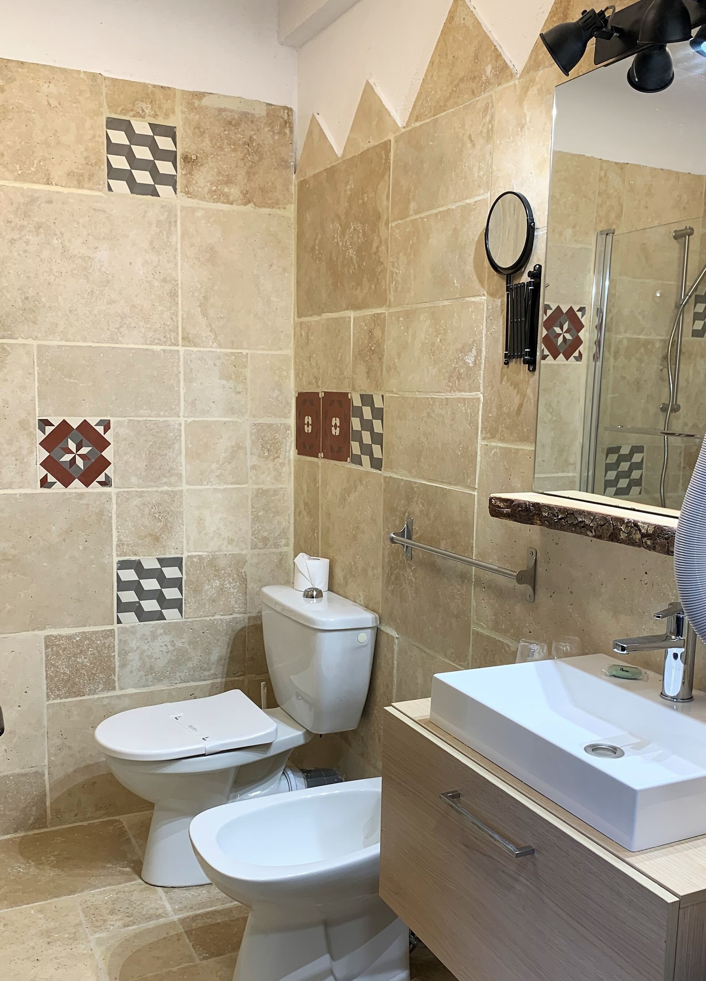 Un baño con dos inodoros, un bidé, un lavamanos, un espejo y una ducha.