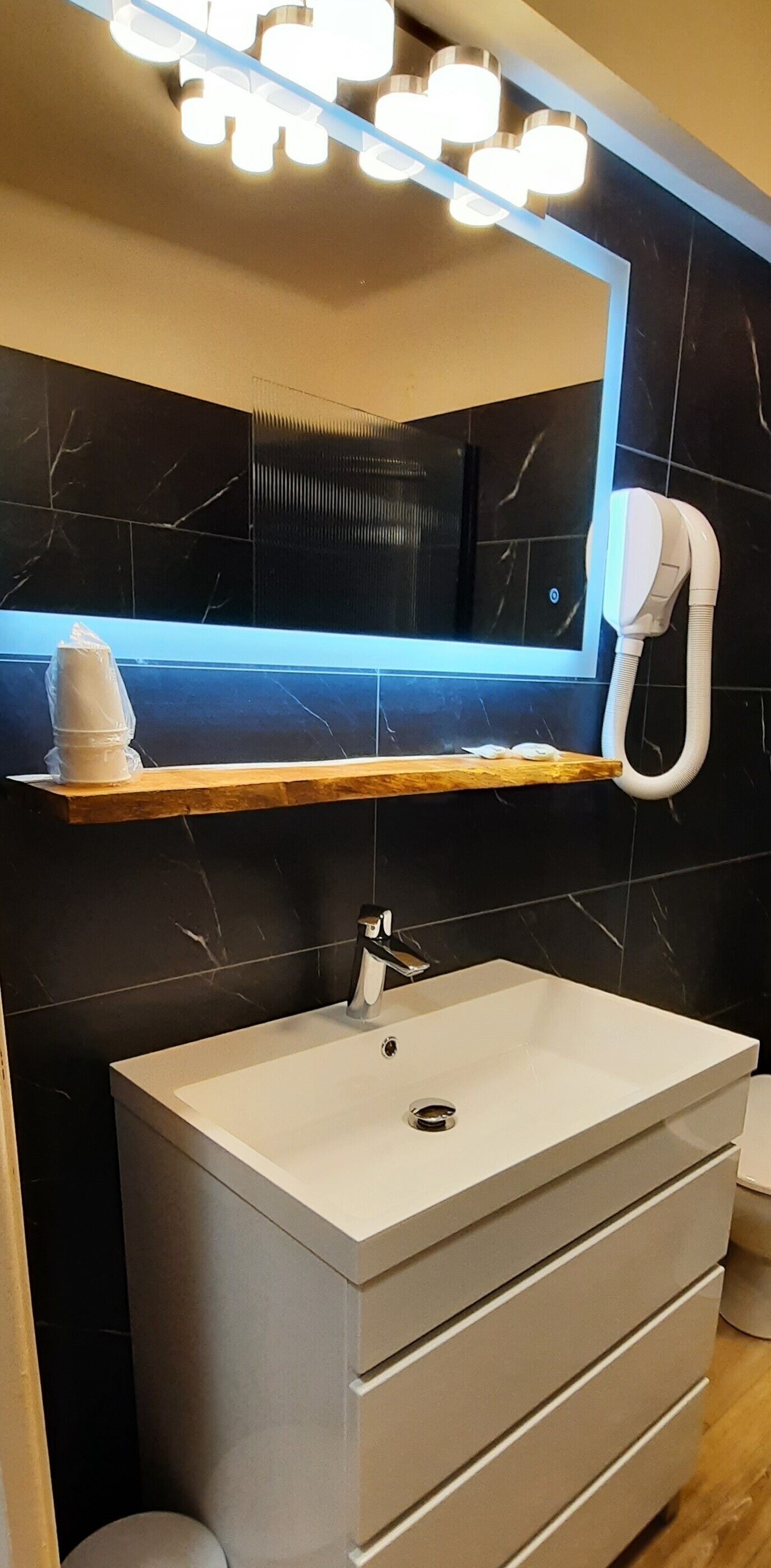 Un bagno con un lavandino bianco, uno specchio sopra e un asciugamano su uno scaffale.