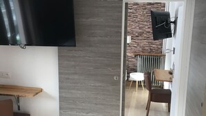 A modern kitchen with a built-in TV, a wooden dining table, and a brick wall in the background.