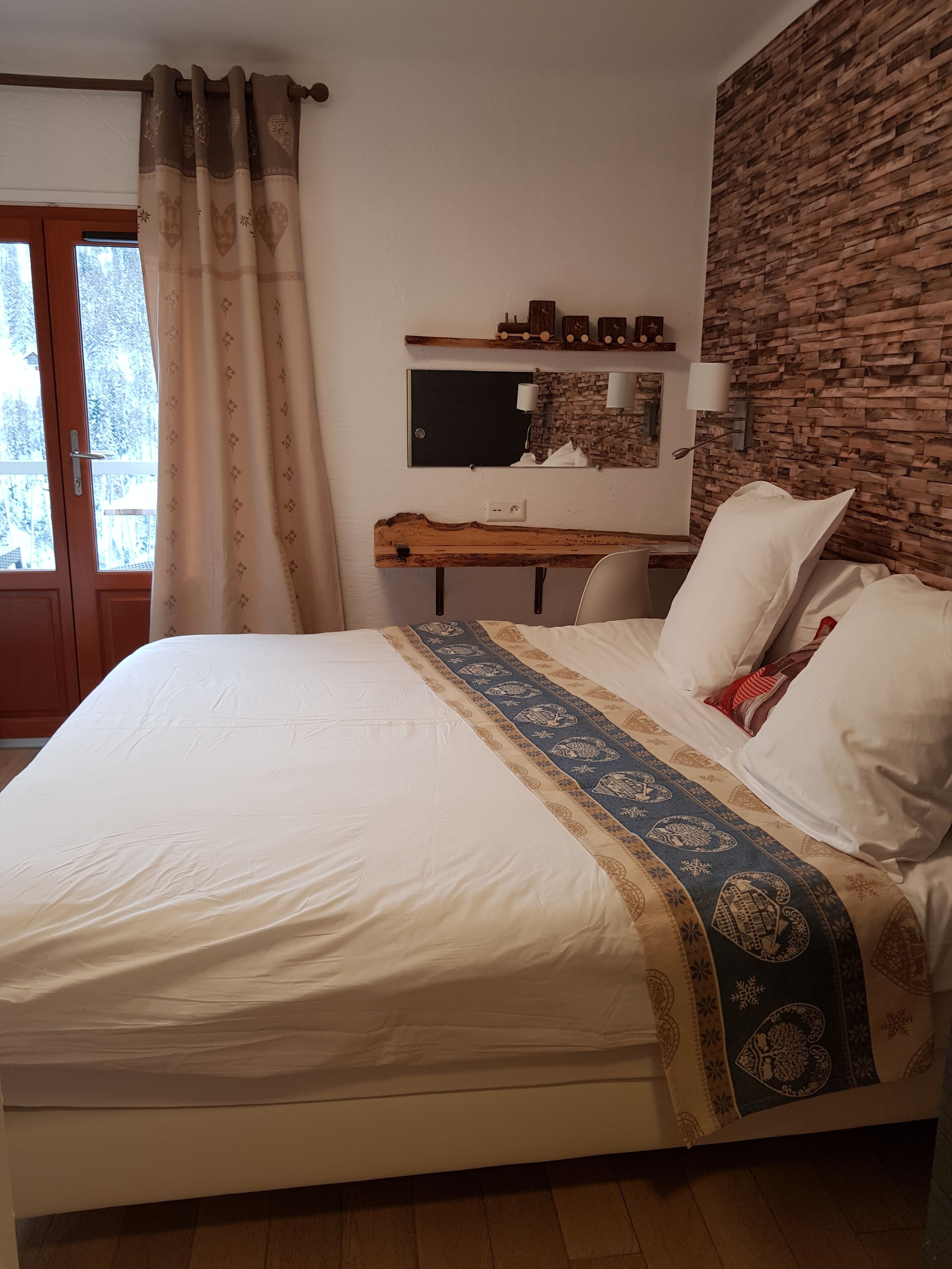 Ein Schlafzimmer mit einem Bett, einem Holztisch, einem an der Wand montierten Fernseher und einem Fenster mit Vorhängen.