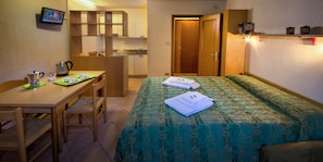 Habitación de hotel con cama, escritorio, silla, kitchenette y televisión.