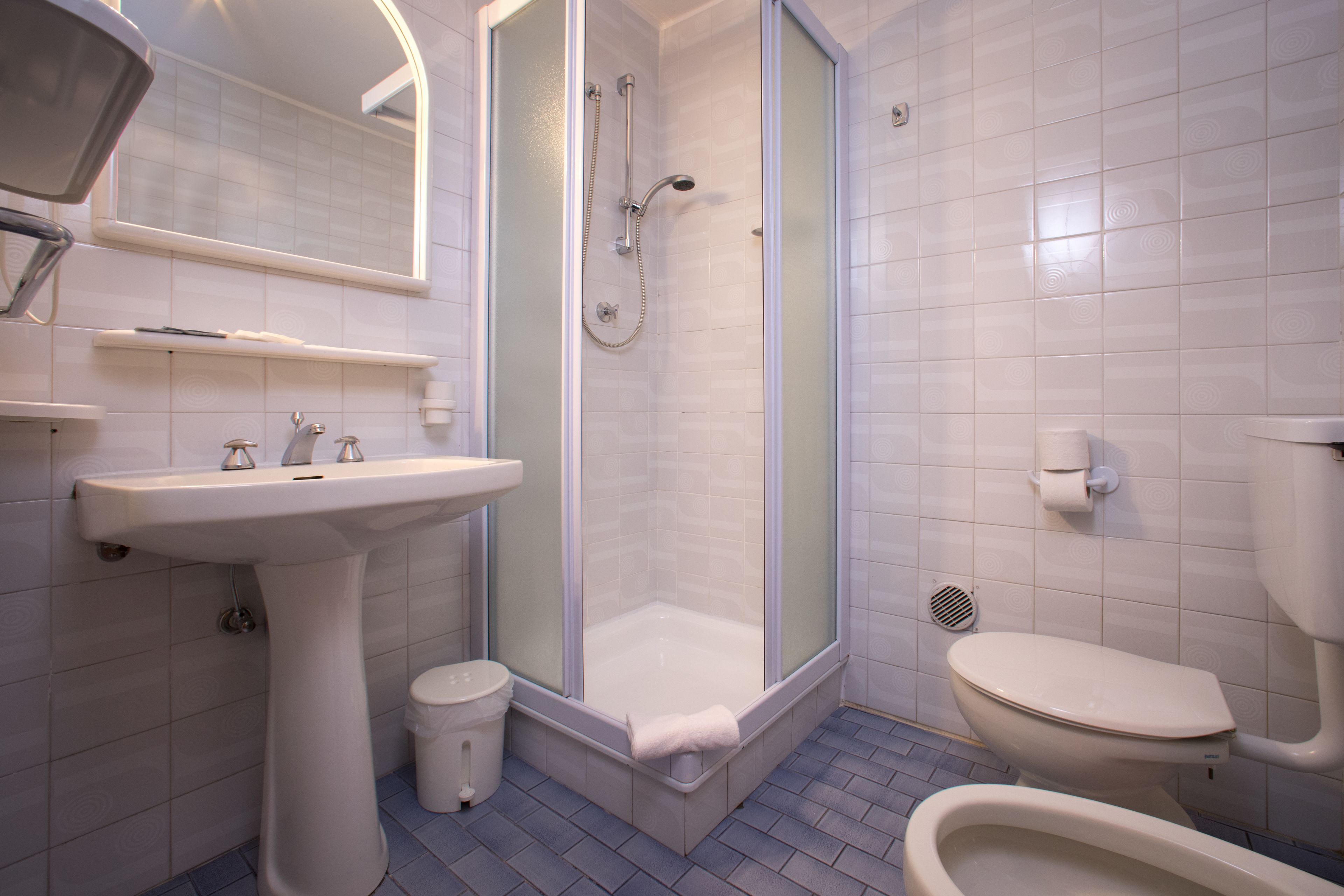 Un baño moderno con ducha de vidrio, lavamanos pedestal y retrete.