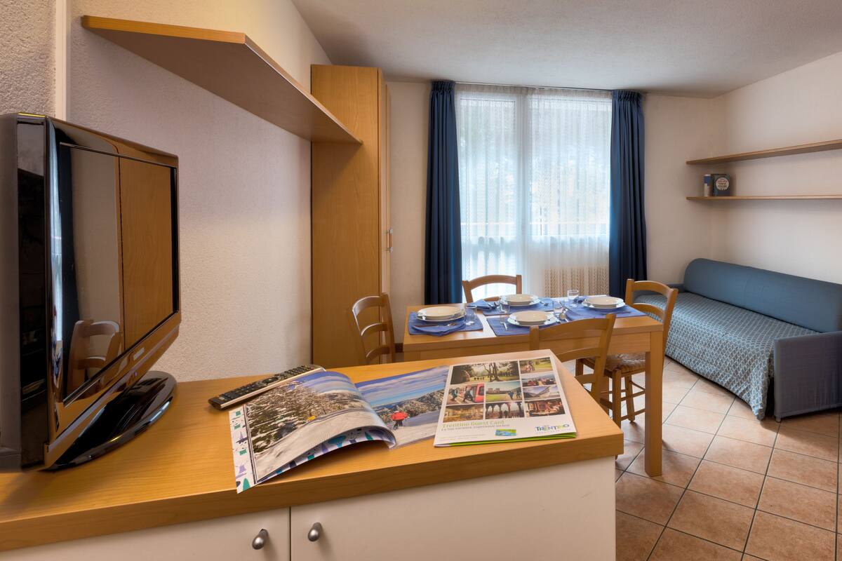 Habitación compacta con escritorio de madera, televisión, mesa de comedor con sillas, sofá y armario.