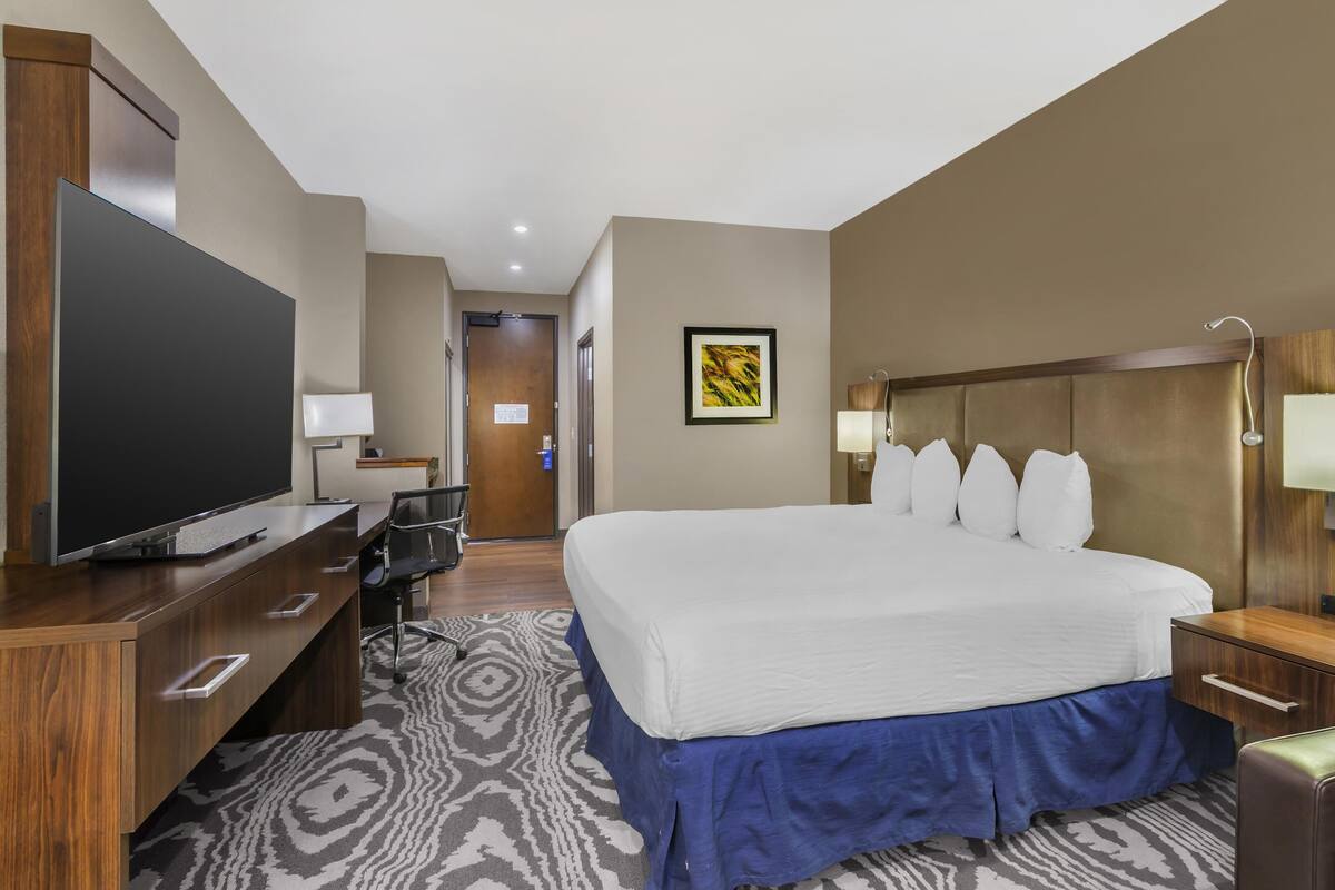 Quarto de hotel com cama grande, televisão de tela plana, escrivaninha e cadeira.