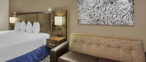 Una habitación de hotel con cama, sofá de cuero marrón, lámpara de pared y un cuadro abstracto grande.