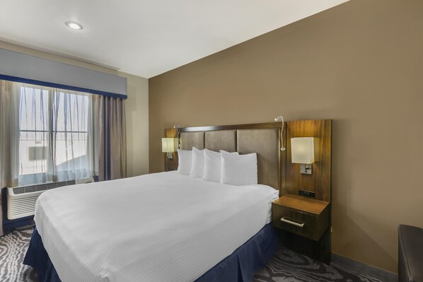 A hotel room with a large bed, a wooden headboard, two bedside tables with lamps, and a window with curtains. - Best Western Plus Williston Hotel & Suites (Williston)