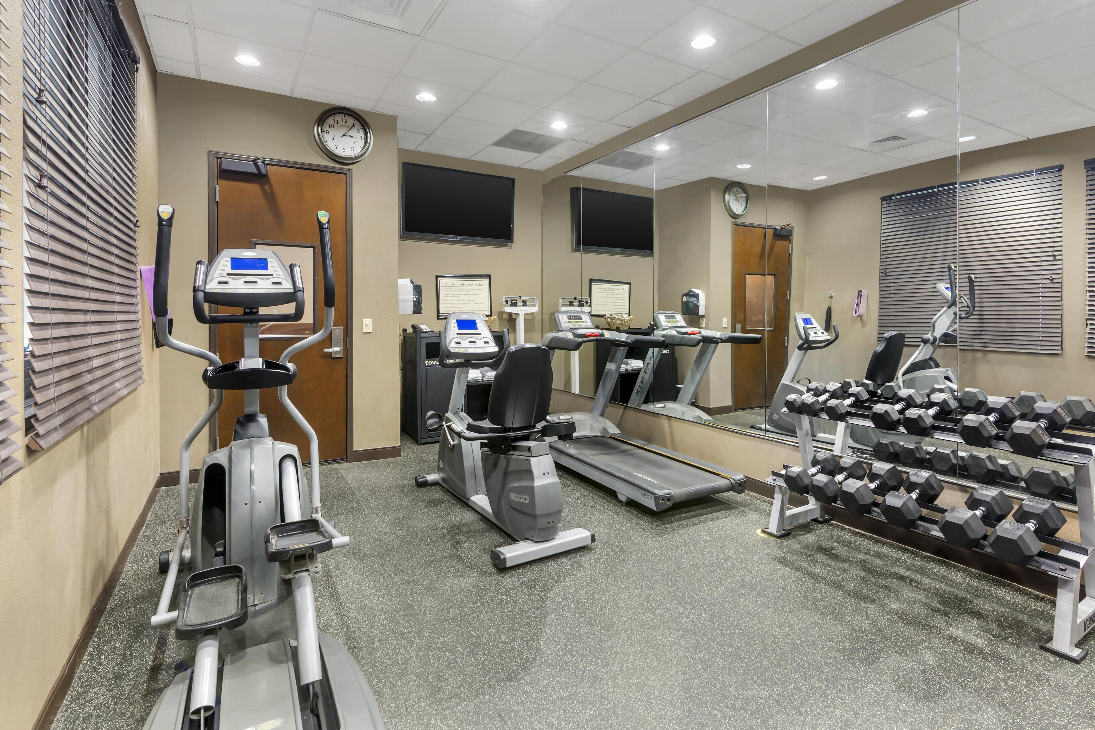 A gym with treadmills, elliptical machines, and a rack of dumbbells.