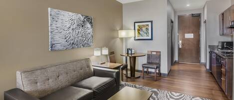 A modern living room with a sofa, a coffee table, and a dining area with a table and chairs. There is a kitchen area with cabinets and a microwave.