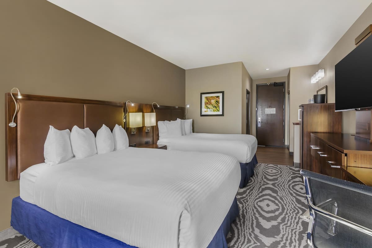 Quarto de hotel com duas camas, uma escrivaninha, televisão e um banheiro ao fundo.