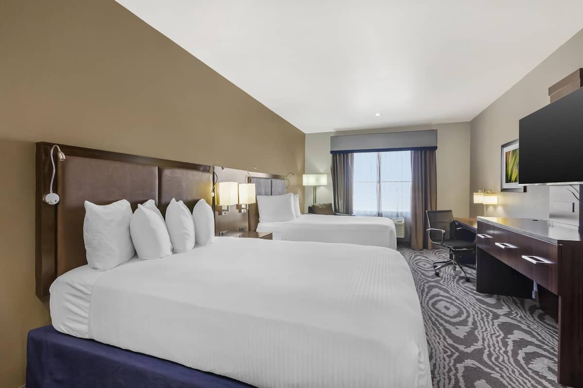 Quarto de hotel com duas camas, uma escrivaninha, uma cadeira e uma televisão.