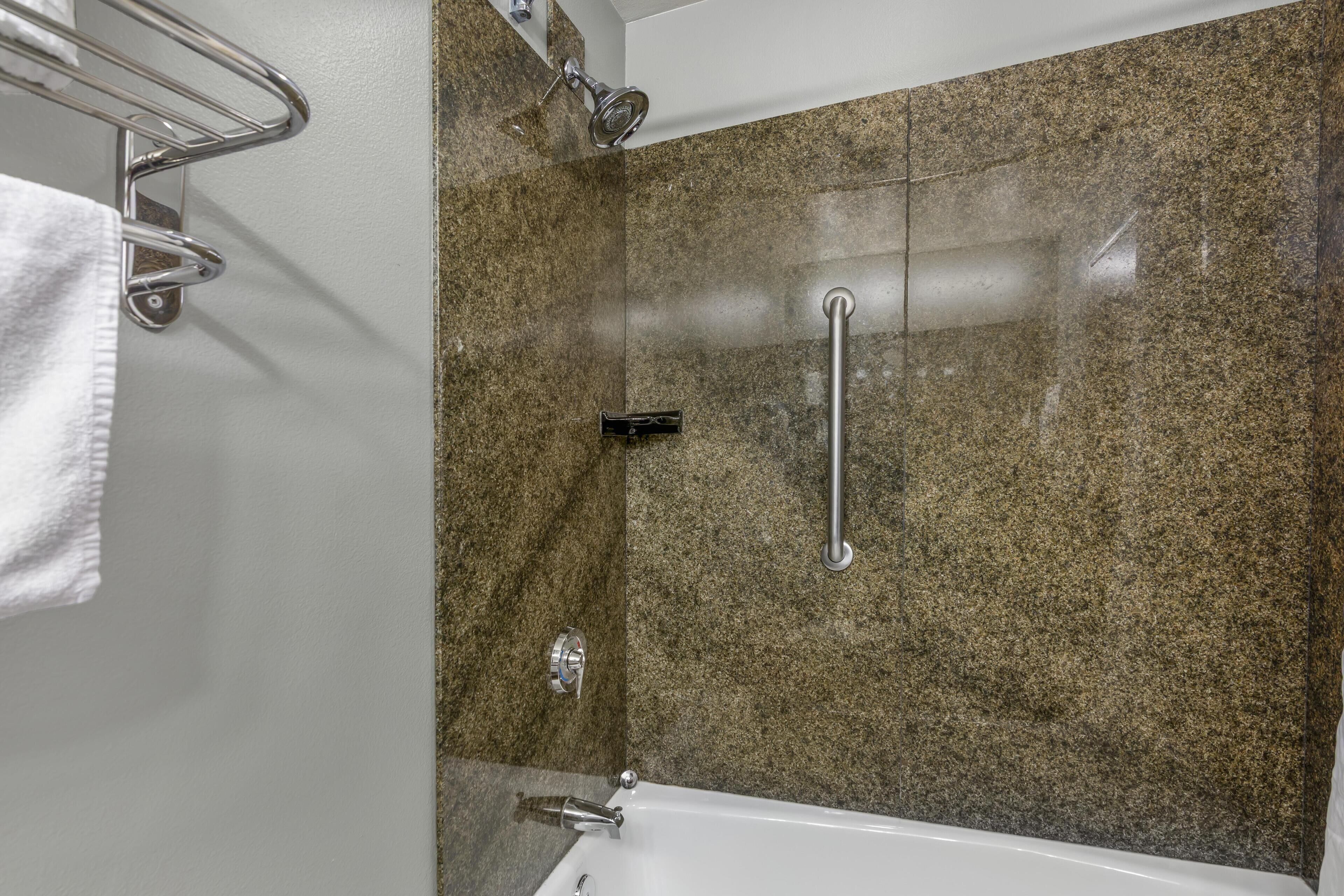 A bathroom with a granite shower wall, a white bathtub, and a towel rack.