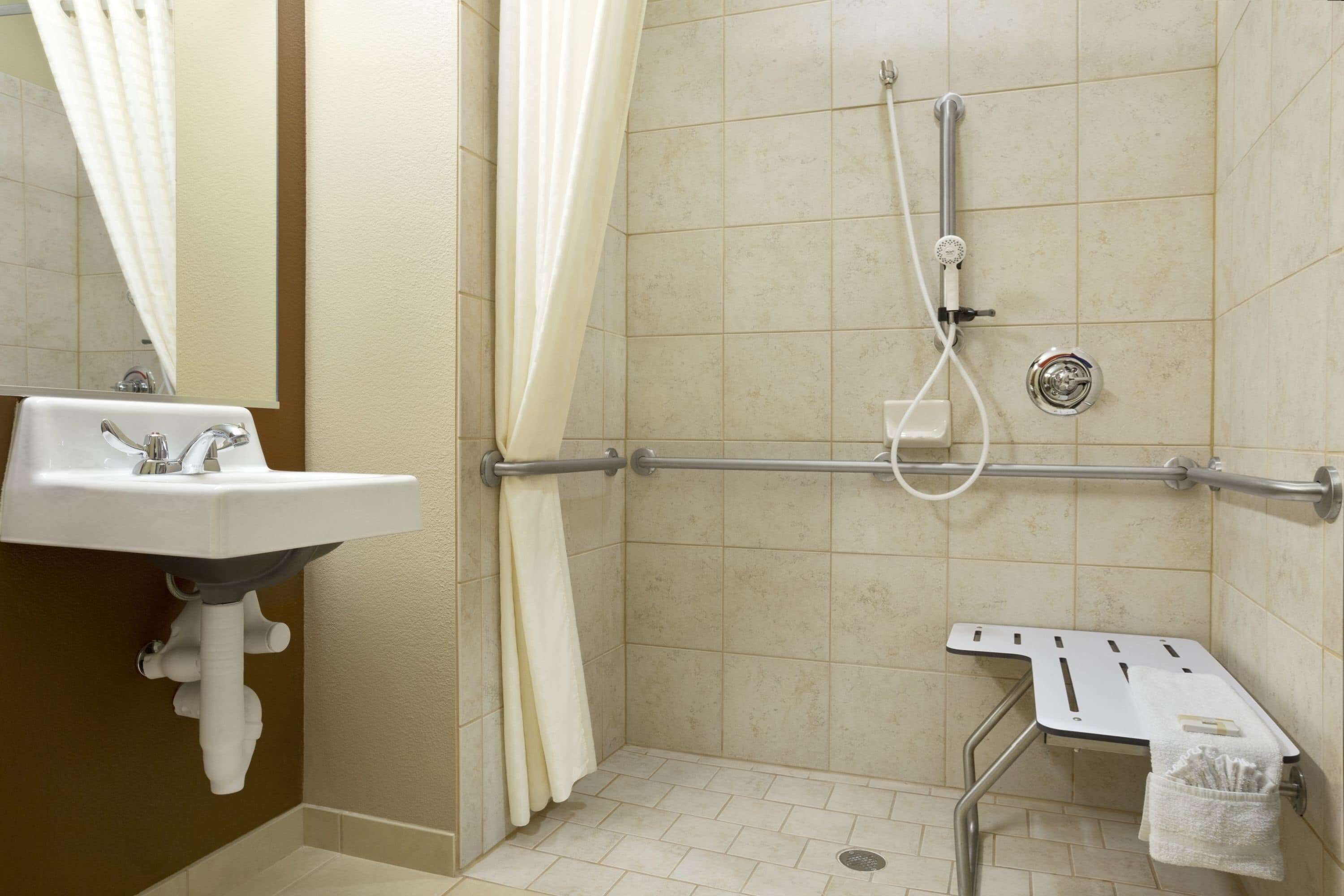 Un baño con lavamanos, ducha y barra de apoyo.