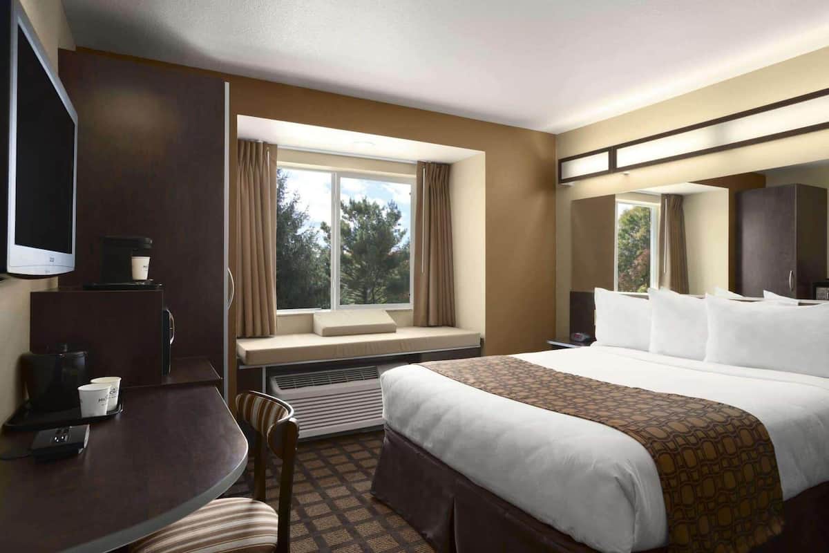 A hotel room with a bed, a desk with a chair, a television, and a window with curtains.