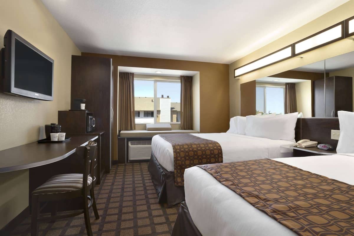 A hotel room with two beds, a desk with a chair, a television, a window with curtains, and a large mirror.