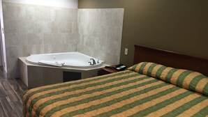 A hotel room with a large bathtub, a bed with striped bedding, and a wooden headboard. - Bellflower Travel Inn (Bellflower)