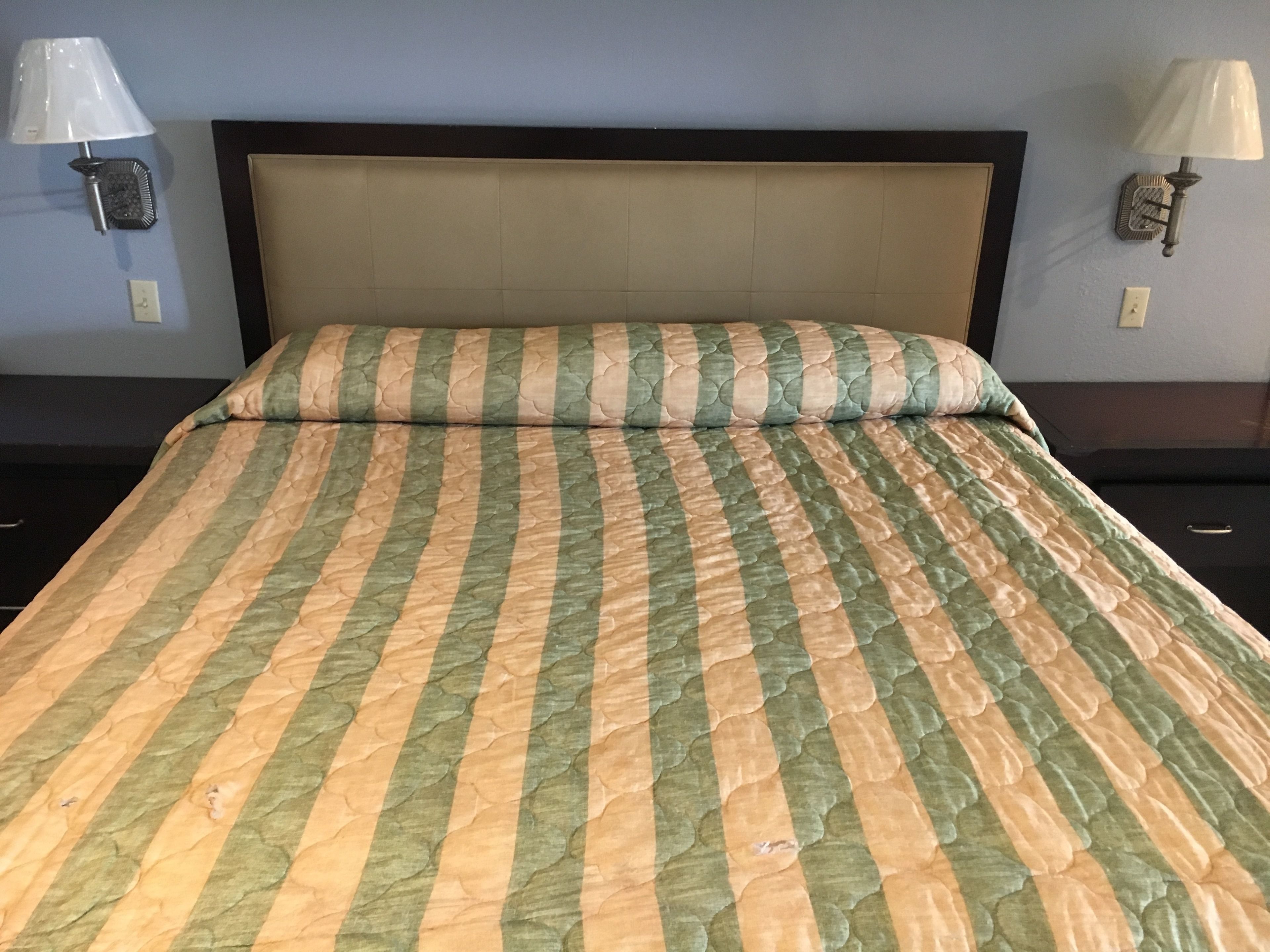 A bed with a striped bedspread, two wall-mounted lamps, and a plain headboard.