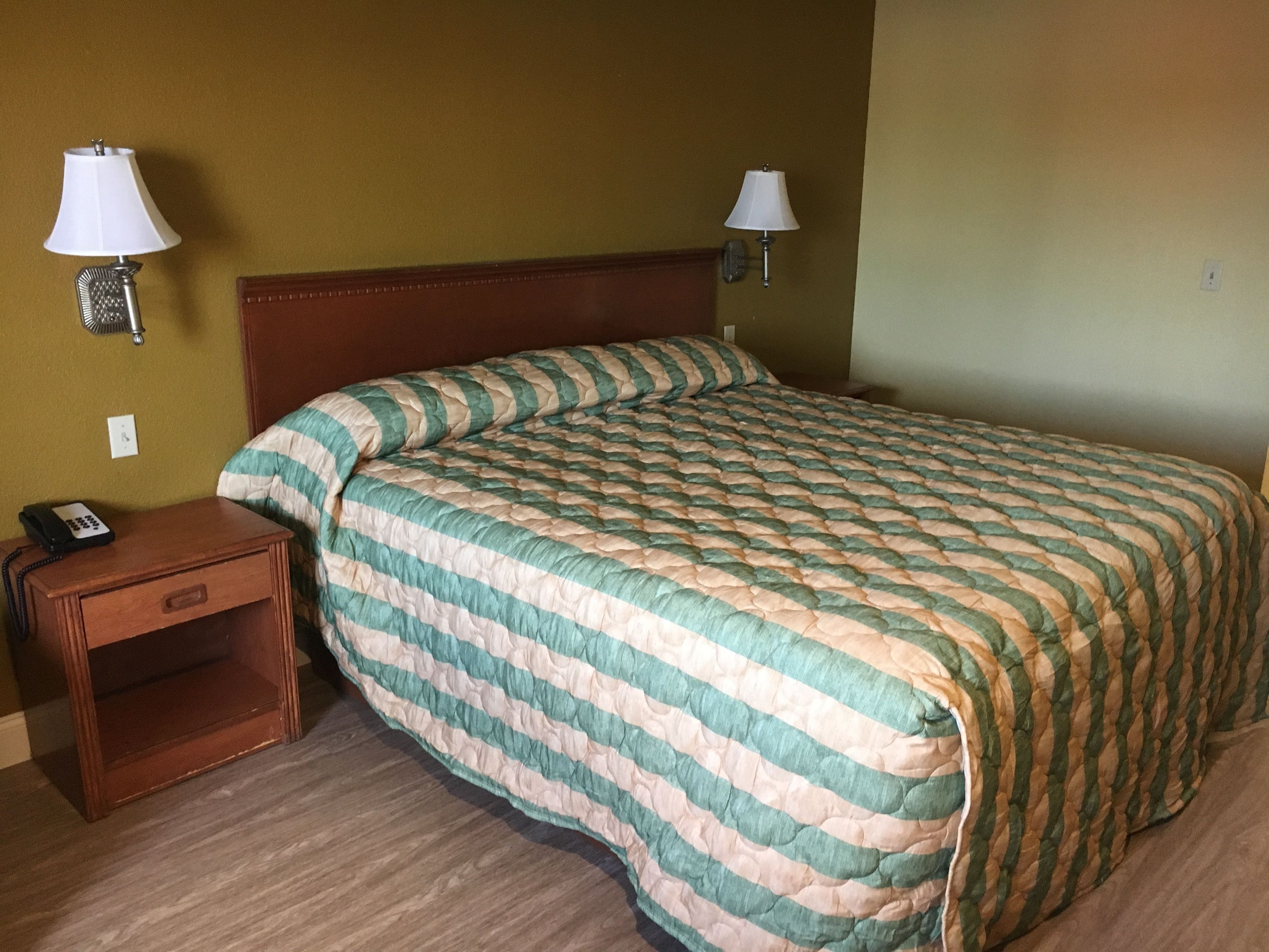 Une chambre d’hôtel avec un grand lit, deux lampes de chevet, une table de chevet en bois avec un téléphone et une prise électrique au mur.