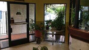 A hotel lobby with a glass door entrance, potted plants, a small table with decorative items, and a framed picture on the wall. - Bellflower Travel Inn (Bellflower)