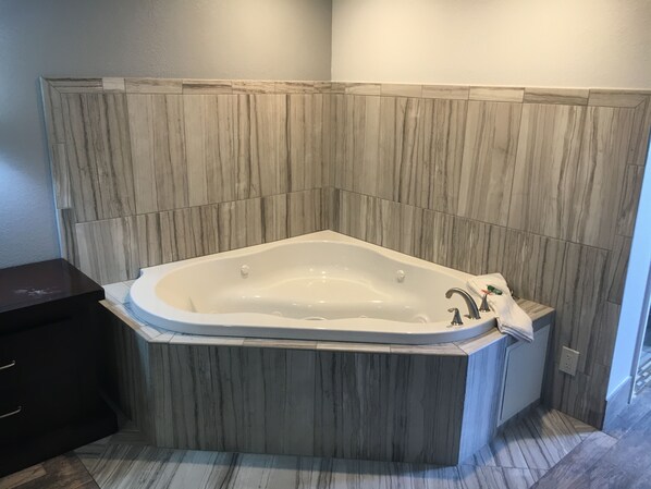 A corner bathroom with a freestanding bathtub, a dark wooden vanity, and a marble-patterned wall. - Bellflower Travel Inn (Bellflower)