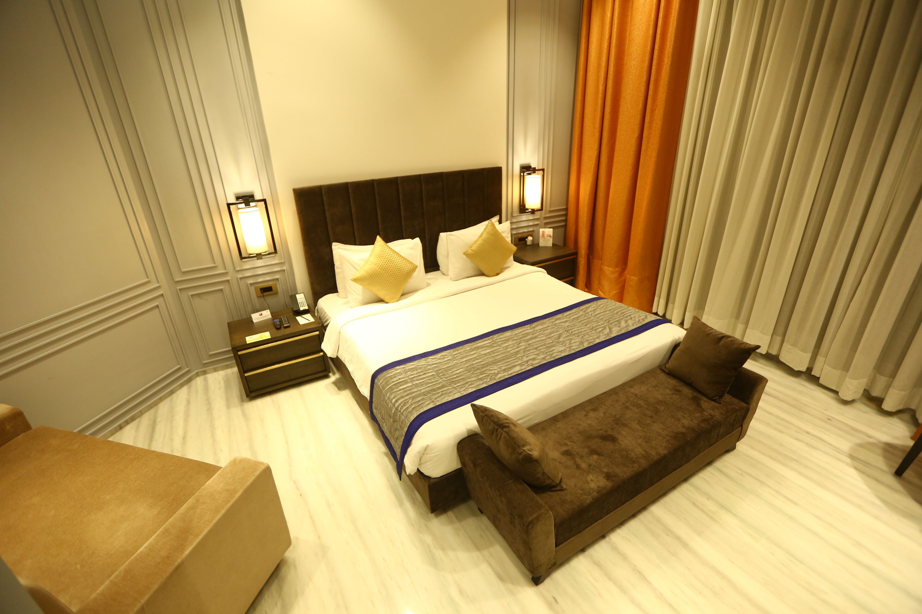 A hotel room with a large bed, a bench, a nightstand, and a lamp.